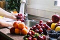 Assortment of fresh red fruit, hands of woman washing a bunch of grape under the water flush, inside the kitchen Royalty Free Stock Photo