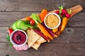 Assortment of fresh vegetables and hummus dip on a serving board, top view on rustic wood Royalty Free Stock Photo