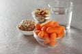 Assortment healthy snacks for dieting: baby carrots, nuts, granola bars and glass of water on table.