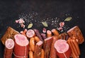 Assortment of meat products including sausage ham bacon spices garlic on a black background view from the top. Boiled