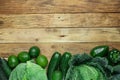 Assortment of Organic Green Vegetables Savoy Cabbage Zucchini Cucumbers Bell Peppers Avocados Arranged in Bottom Border on Wood