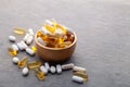 Assortment scattered pharmaceutical medicine vitamins, pills, drugs in wooden bowl on gray background. White food dietary