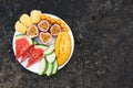 Assortment of sliced tropical fruits on plate. Background of dark stone. Royalty Free Stock Photo