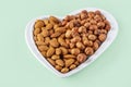 Assortment of various types of nuts - hazelnuts,  almonds in heart shaped plate on green background. Healthy vegetarian snacks. Royalty Free Stock Photo