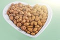 Assortment of various types of nuts - hazelnuts,  almonds in heart shaped plate on green background. Healthy vegetarian snacks. Royalty Free Stock Photo