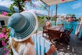 Assos village, Kefalonia, Greece. Female tourist in blue sunhat in front of cozy veranda terrace door admiring turquoise Royalty Free Stock Photo