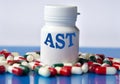 AST - medical acronym on a white jar against the background of randomly scattered tablets