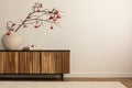 Asthetic composition of japandi living room interior with copy space, wooden sideboard, round vase with red rowan, books, bright