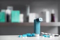 Asthma inhaler and pills on table against blurred background.