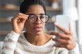 Astigmatism. Young Black Female In Eyeglasses Trying To Read Message On Smartphone Royalty Free Stock Photo