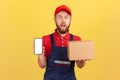 Astonished courier holding cardboard box and smart phone with empty screen. Royalty Free Stock Photo