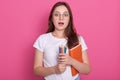 Astonished dark haired woman with opened mouth, carries textbook and colored pencils for writing or drawing, being ready to make