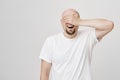 Astonished and excited bald bearded man with broad smile covering eyes with hand and awaiting for something positive to