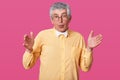 Astonished man shows large or wide object, wears modern bright shirt with white bowtie, has amazed facial expression. Pensioner Royalty Free Stock Photo
