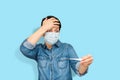 Astonished sick woman in medical mask looking with expression at thermometer in hand on light blue background