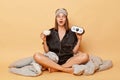 Astonished surprised young girl sitting floor with blanket wears black pajama and sleep eye mask holding alarm clock and cup of Royalty Free Stock Photo