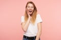 Astonished young pretty female with loose foxy hair holding raised palm on her cheek while looking excitedly at camera with wide