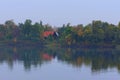 Astonishing landscape of autumn colored trees are reflected in the water. Wooden house with red tile roof is hidden in the forest Royalty Free Stock Photo