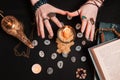 Astrology and esotericism. Female witch hands divination over a candle. On a black background lie fortune-telling runes, a book,