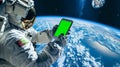 Astronaut using green screen phone while performing spacewalk in open space. Planet Earth on background. Chroma key