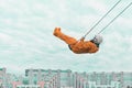 Astronaut wearing orange space suit and space helmet flying on a swing against cloudy sky above the cityscape Royalty Free Stock Photo