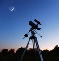 Astronomical telescope is pointed at the moon. Blue clear night sky. Silhouette of a astronomy telescope with twilight sky