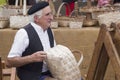 Asturias, Spain - 4 August 2019 : artisan having a conversation while making a wooden basket in a traditional market. old man