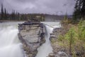 Athabasca Falls in the Rocky Mountains of Canada. Between the cliffs above the water stuck logs. Cloudy day in Jasper Royalty Free Stock Photo