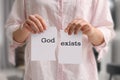 Atheism as religious position. Woman ripping paper with text God Exists indoors, closeup