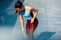 Athelte female working with elastic band outside on grey background. Healthy fit woman exercising with resistance band on a sunny