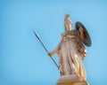 Athena marble statue with helmet, spear and shield under clear blue sky.