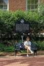 A young woman looks at her mobile phone while sitting on an ornate cast iron bench in front of a historic brick building