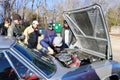 A group of men look under the hood of a classic car at an outdoor show