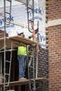 A bricklayer standing on scaffolding works a length of steel angle stock with a trowel