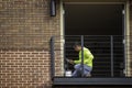 A painter kneels to apply paint to an open balcony door on a new brick building