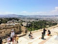 A group of tourists taking photos on a summer day on top of the Acropolis with the sprawling city of Athens, Greece