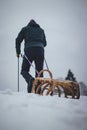 Athlete in black winter clothes pulls to the top of the slope a wooden sledge for a quick ride down and experience a piece of