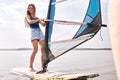 female stands on windsurf and holds the sail. Windsurfing on lake water, relaxing on water.