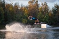 An athlete does a trick on the water. A rider jumps on a wakeboard against a background of a green forest. Sunset on the lake