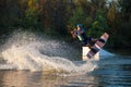 An athlete does a trick on the water. A rider jumps on a wakeboard against a background of a green forest. Sunset on the lake Royalty Free Stock Photo