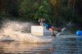 An athlete does a trick on the water. A rider jumps on a wakeboard against a background of a green forest. Sunset on the lake