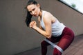 An athlete female working with the elastic band outside on grey background. Healthy fit woman exercising with resistance band on a