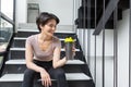 Athlete girll sitting in a black tight-fitting sports suit with a drinking bottle and sitting on the stairs