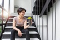 Athlete girll sitting in a black tight-fitting sports suit with a drinking bottle and sitting on the stairs