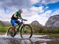 An athlete guy crosses a mountain river on a bicycle