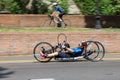 Athlete with its Special Bike on a City Track during a Race and a Cyclist on a Road Bike Just Above