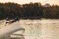 An athlete jumps over the water. Wakeboard park at sunset. Rider performs a trick on the board