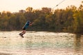 An athlete jumps over the water. Wakeboard park at sunset. Rider performs a trick on the board