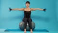 Athlete lifting dumbbells and sitting on fitness toning ball