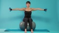 Athlete lifting dumbbells and sitting on fitness toning ball